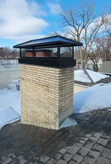 Buff brick chimney in winter with a black multi-flue chimney cap covering the whole top