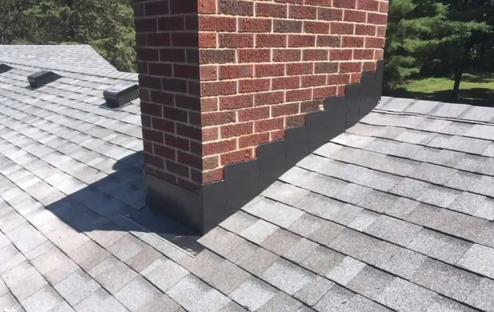 Red brick chimney on a grey shingle roof with new black step flashing where the brick meets the shingles